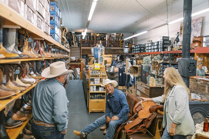 Rhe’Ann McBride and her dog, Finley, wait as JW Simonson, a rancher from Dunning, picks out a pair of boots.